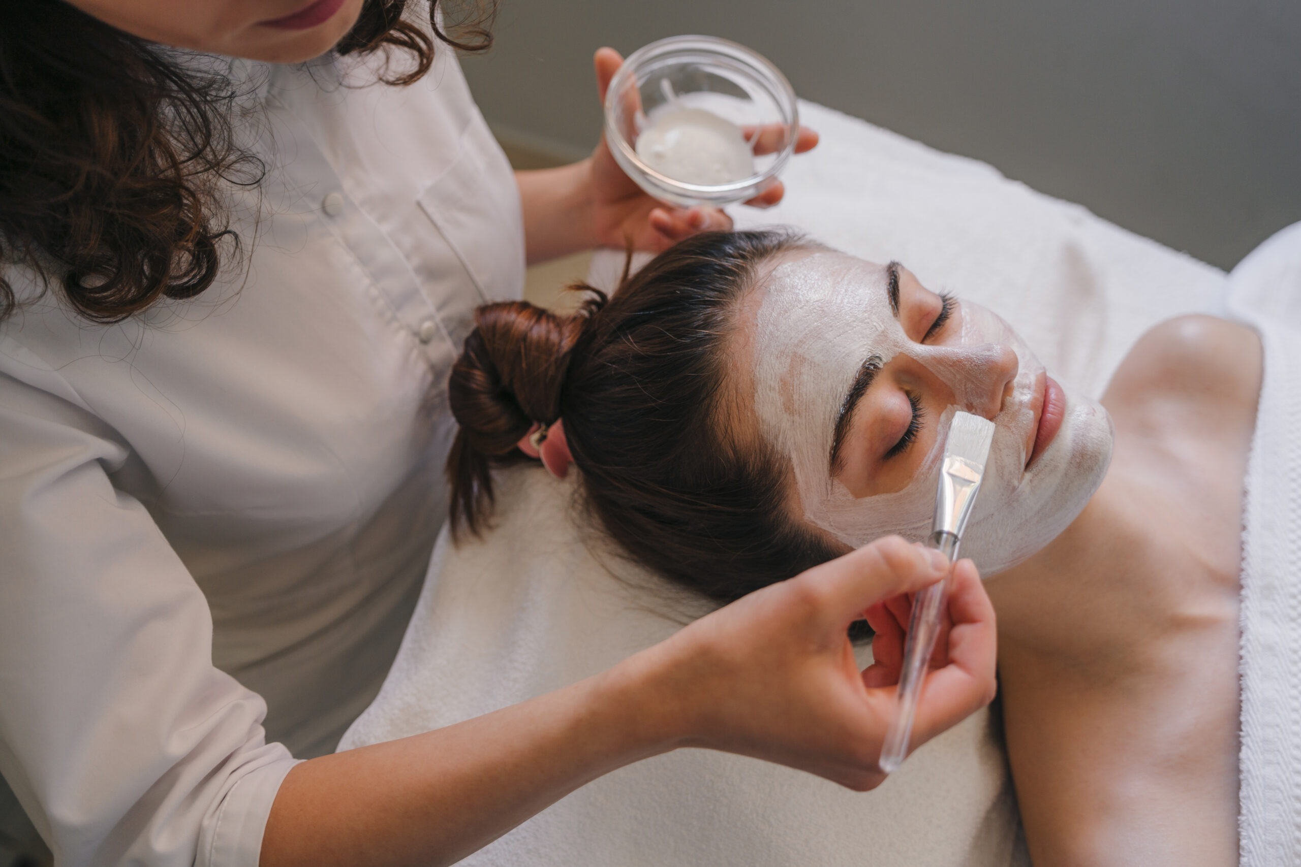 Cosmetologist applying facial cream all over young woman's forehead at spa salon. Skin treatment. Girl facial treatment. The Laser Room Facials Loyalty Program